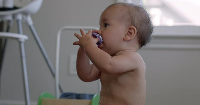 1 year old baby puts toy in mouth sitting alone in kitchen - close up slow motion