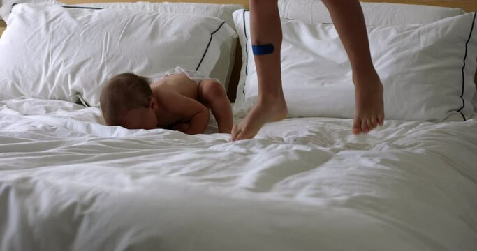 Older brother jumps on parents bed as baby sister bounces and laughts - family sibling love fun