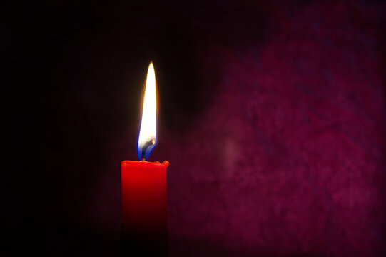 Single red candle burning alone in the dark red