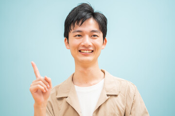 ブルーバックで指さしをするジャケットを着た若い日本人男性