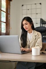 Beautiful Asian businesswoman focused on her project assignment, working, using her laptop