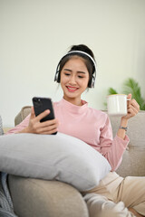 Pretty Asian girl chilling in her living room, listening to music through headphones