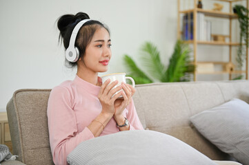 Calm Asian female listening podcast or music through her headphones while sipping tea