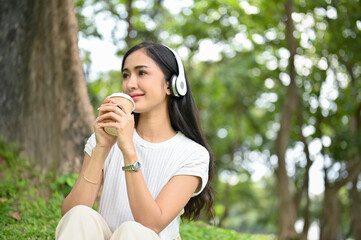 Attractive Asian female listening to music and sipping coffee while relaxing in park.