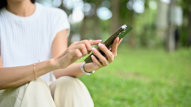 Chilling Asian female using her mobile phone while relaxing in the park. cropped image