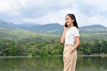 Confident Asian businesswoman talking on the phone while walking around the lake.