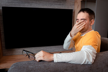 fatigue of vision . A viewer in a yellow shirt on the background of the TV. man feeling tired,...