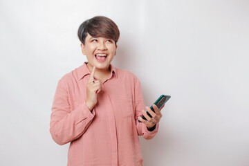 Fototapeta premium A portrait of a happy Asian woman is smiling and holding her smartphone wearing a pink shirt isolated by a white background
