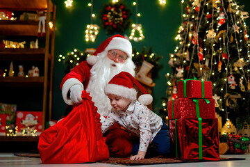 Fototapeta na wymiar Little boy in Santa's hat takes out presents from Santa claus sack. Christmas time. New Year concept