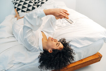 Young mixed race woman looking at cellphone browsing through social media lying upside down on the...