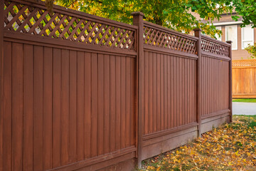 Nice wooden fence around house. Wooden fence with green lawn and autumn leaves.