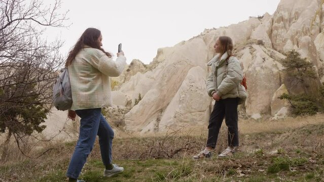 Mother takes pictures photo on smartphone of her daughter against of sandy mountains. Family holidays, hiking, trip vacation. Girl posing to camera. Cappadocia valley