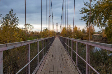 Suspension pedestrian bridge across the Chagan River in Kazakhstan. Suspension bridge in autumn.