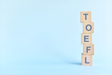 TOEFL or test of english as a foreign language testing system exam concept. Wooden blocks typography flat lay on blue background.	