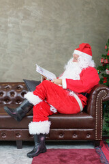 Senior man in Santa Claus costume reading newspaper on sofa in the living room at home