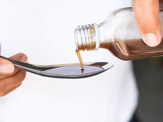 Hand holding Cough Medicine Pour in Spoon close up ,Sick Problem,Medicine in Hospital concept.