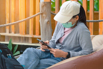 Female tourist wear cap and face mask with backpack use mobile phone to search for attractions...