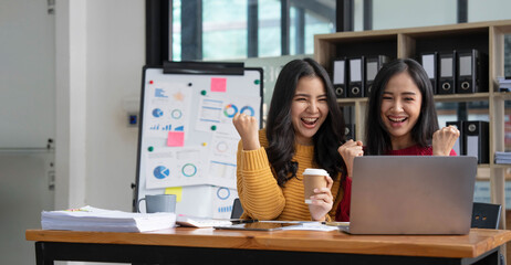 Two young Asian businesswomen show joyful expression of success at work smiling happily with a...