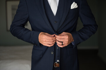 Groom getting ready for wedding buttoning navy suit jacket  close crop no face