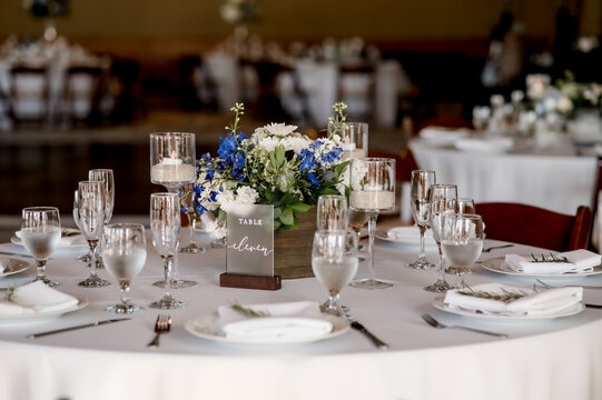 Table Eleven sign on table with blue and white wedding floral centerpiece on white table cloth surrounded by place settings and glassware