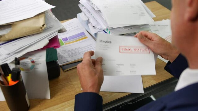 A man opening a stack of bills and letters with overdue notice for an invoice