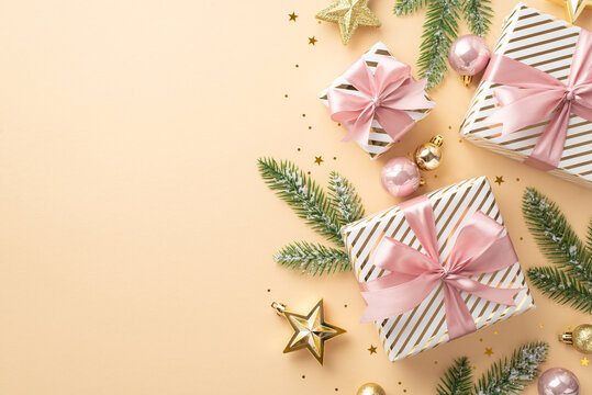 Christmas atmosphere concept. Top view photo of present boxes with ribbon bows gold and pink baubles star ornaments fir branches in frost and confetti on isolated light beige background with copyspace