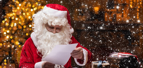 Workplace of Santa Claus. Cheerful Santa is reading letters from children while sitting at the...