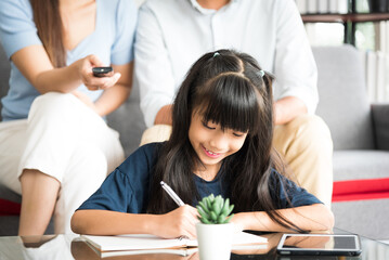 Portrait of happy daughter sitting and doing her homework relaxing with her family at home.