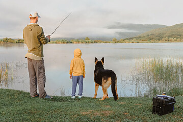 Dad, son and dog are fishing on the lake in the morning.