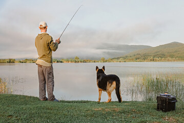 A man and dog are fishing on the lake in the morning.