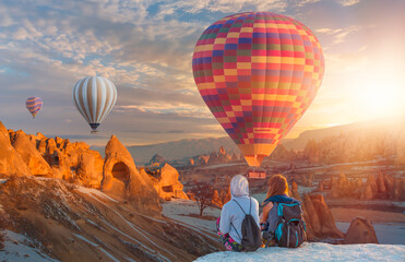 Hot air balloon flying over spectacular Cappadocia - Girls watching hot air balloon at the hill of...
