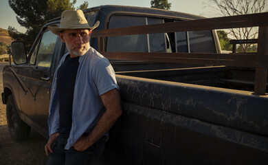 Portrait of adult man in cowboy hat standing against a vintage truck during sunset - Powered by Adobe
