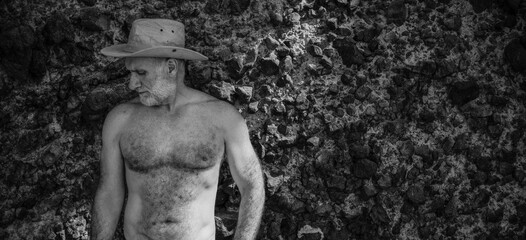 Monochrome of shirtless adult man in cowboy hat against rock