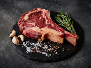 Raw dry aged beef tomahawk steak on slate board with spices for grill. © FoodAndPhoto