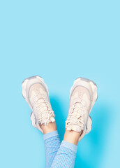 Female legs in trendy sneakers upside down close-up on blue background.