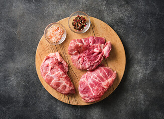 Raw pork cheeks meat on a dark gray surface with spices. Top view. Food background