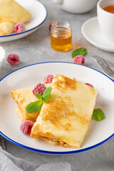 Traditional thin pancakes or crepes with cottage cheese, honey, sour cream and raspberries with cup of tea on a gray concrete background. Food for Maslenitsa. Copy space