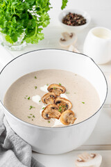 Mushroom cream soup with cream, croutons and herbs on a white wooden background. Delicious comfort food.