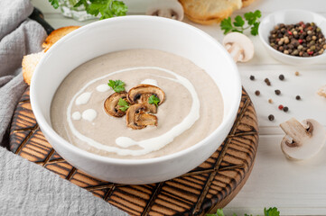 Mushroom cream soup with cream, croutons and herbs on a white wooden background. Delicious comfort food.