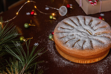 On a wooden brown table lies an apple charlotte sprinkled with powdered sugar. Flat lay top view.