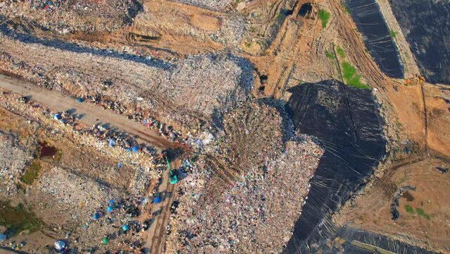 4K : Aerial view from a drone flying over a large pile of garbage, garbage dump with plastic bags. workers and machines are working. Environmental pollution.
