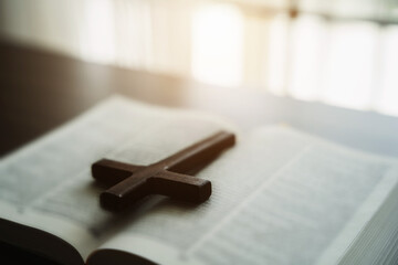 Close up of an open bible with a cross for morning devotion on a wooden table with window lights.
