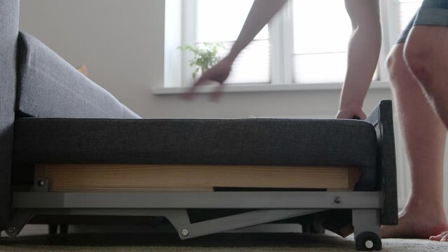 A man folds a convertible sofa in a bedroom at home. Modern upholstered furniture.