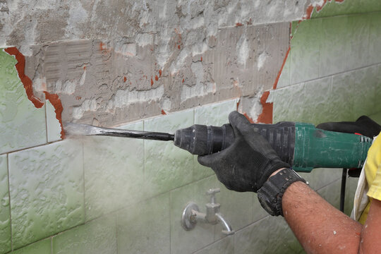 Worker remove, demolish old tiles from wall using electric hammer and chisel in a bathroom or kitchen