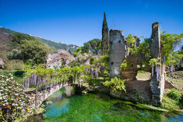 View of the river Ninfa among trees and ruins in spring in Garden of Ninfa, Lazio, Italy - obrazy, fototapety, plakaty