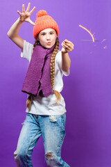 Celebration Ideas. One Expressive Winsome Caucasian Girl in Coral Winter Warm Hat and Violet Knitted Scarf Having Fun With Vivid Bright Burning Bengal Light Fireworks Over Purple Background.