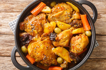 Salvadoran chicken stew with chicha, prunes, carrots, potatoes, olives and onions close-up in a frying pan on a wooden table. Horizontal top view from above