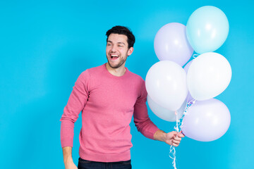 Smiling Happy Caucasian Guy Handsome Brunet Man With Bunch of Colorful Air Balloons in Pink Jumper Standing Over Blue Background.