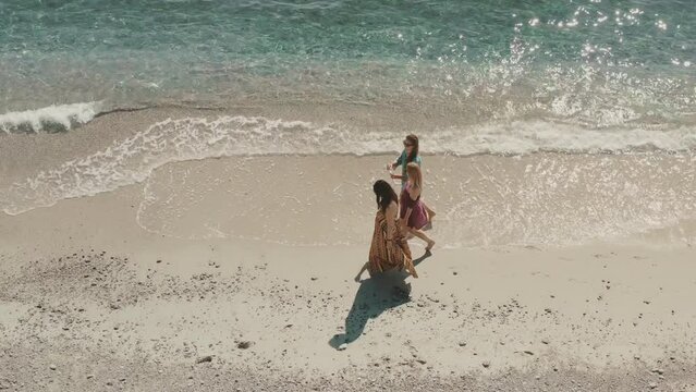 Aerial view of a group of beautiful girls strolling by the sea in the summer morning light in front of a crystal-clear waters in Isca sullo Ionio, Calabria, Italy.