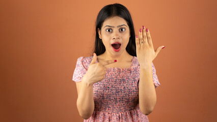 Beautiful excited young Indian woman wearing dress standing isolated over color background, showing...